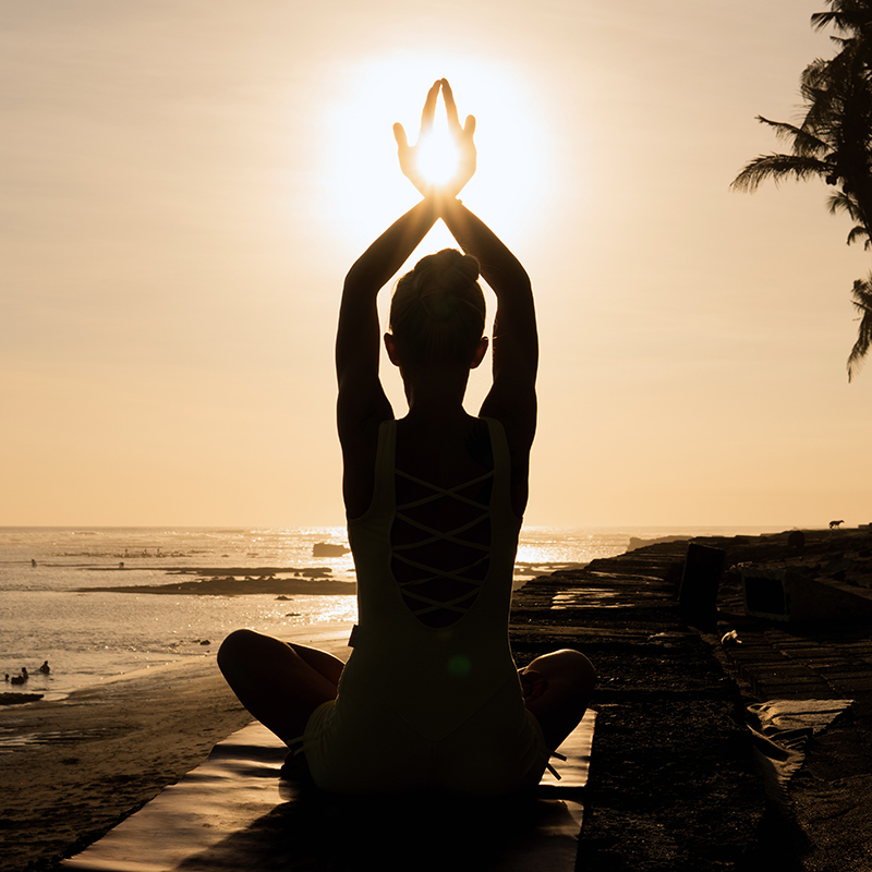 Picture of a woman performing a meditative yoga stance on a coastline at sunset.