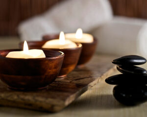 Three candles aligned in a row next to meditation stones in a yoga studio.